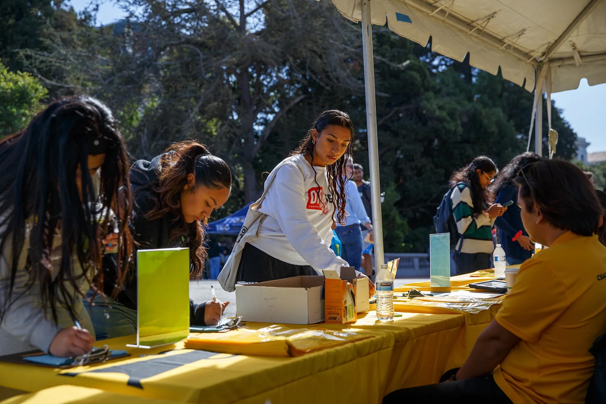 Female students behind a desk outdoors.