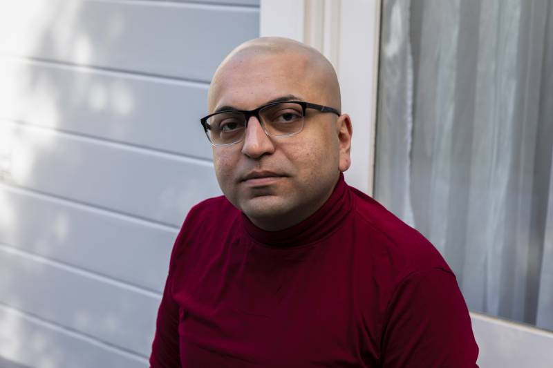 A person with a bald head and wearing glasses looks at the camera.