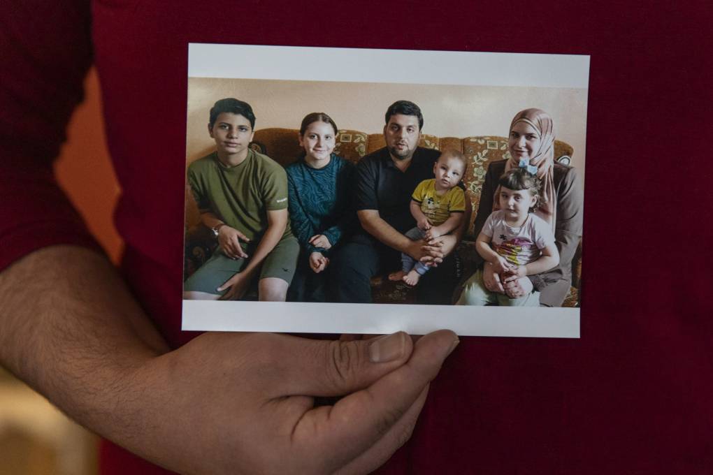 A hand holds a photo of a family sitting on a sofa.