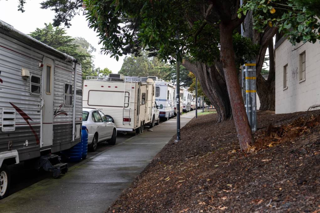 A line of RVs and cars parked on a street.
