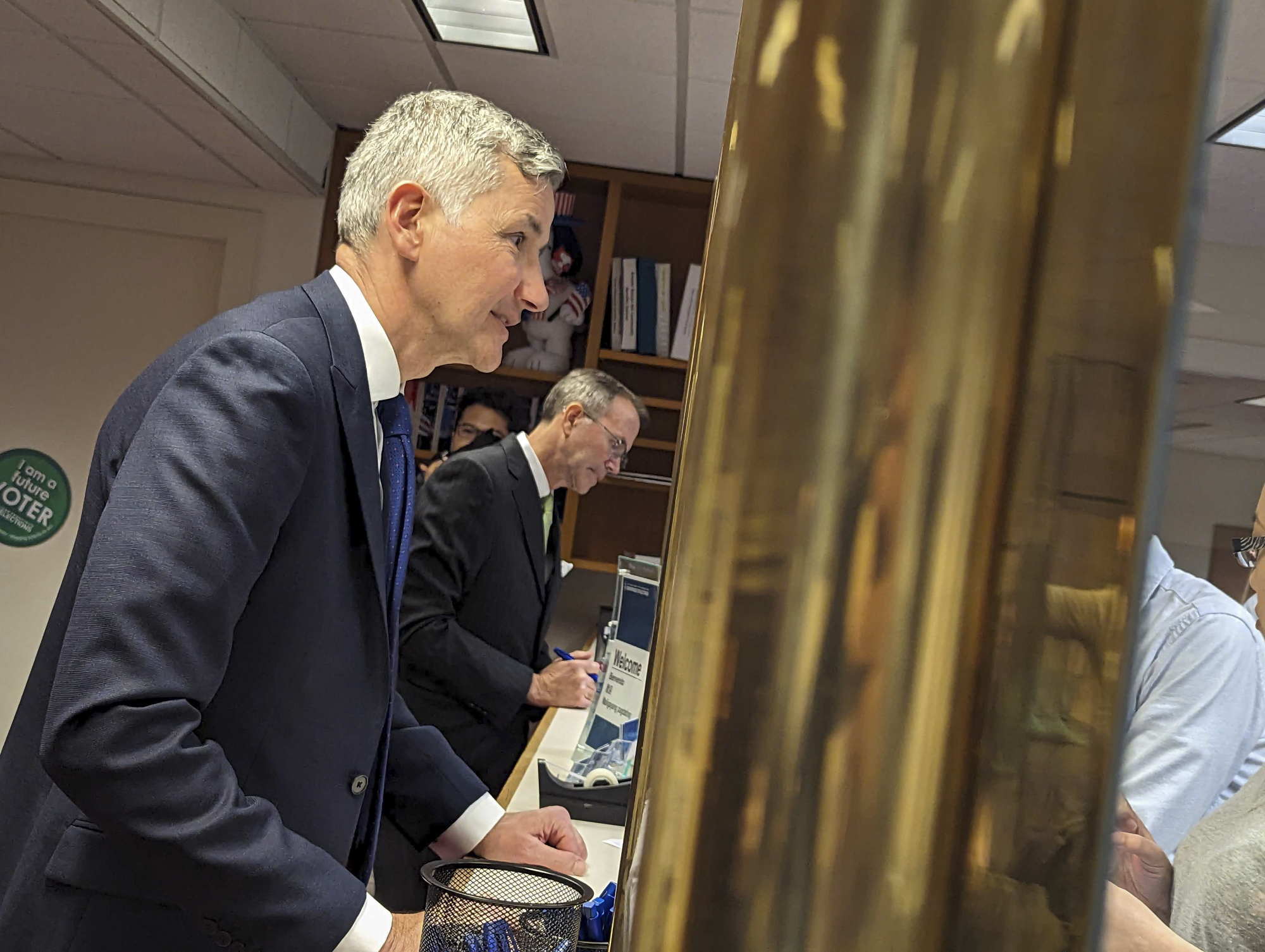 Two white, middle-aged men wearing blue suits are seen from the side as they register.