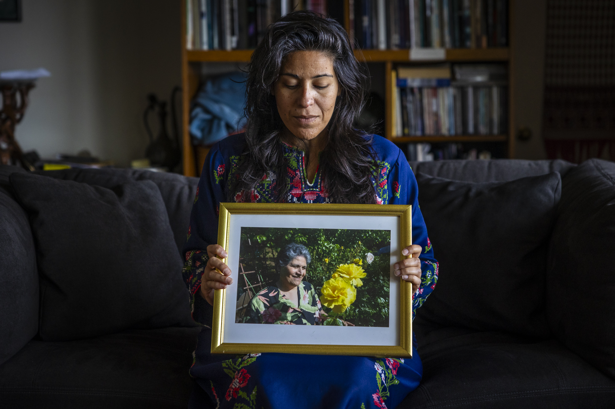 A person with long hair looks down at a framed photo of a person beside two large yellow roses.