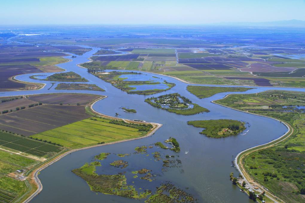 An aerial photo of a large river surrounded by flat, green farmland