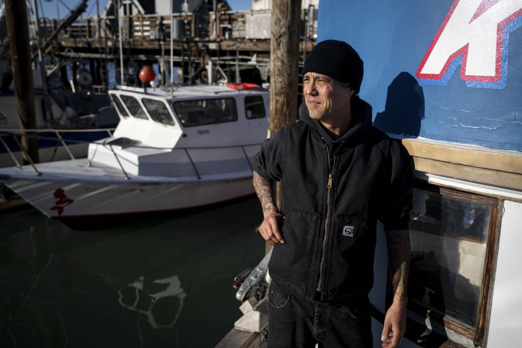 A person in a black beanie stands on the prow of a boat.