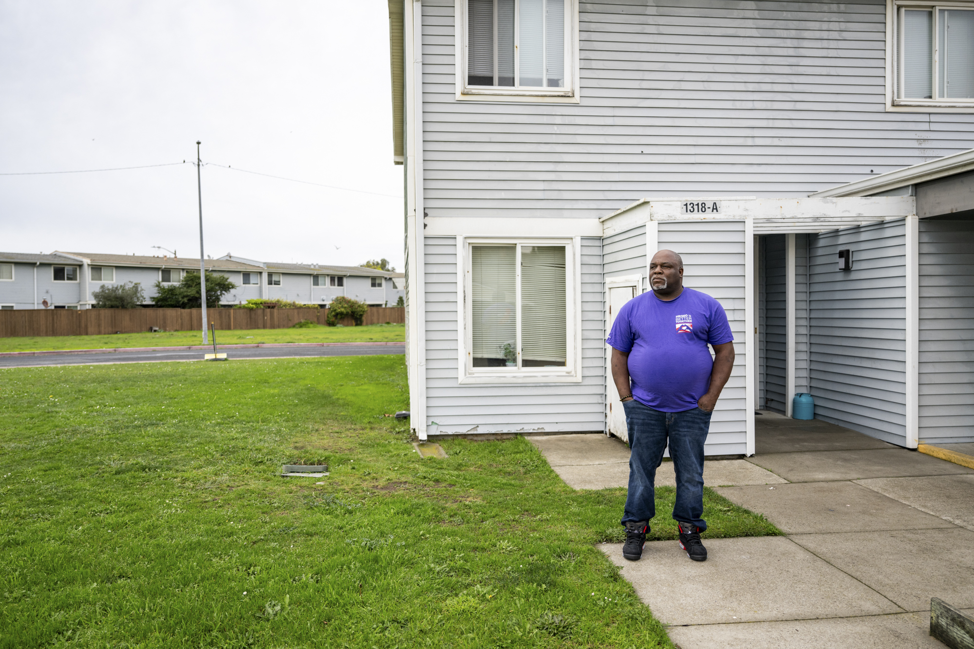A person with a bald head stands in front of a building in a residential area.