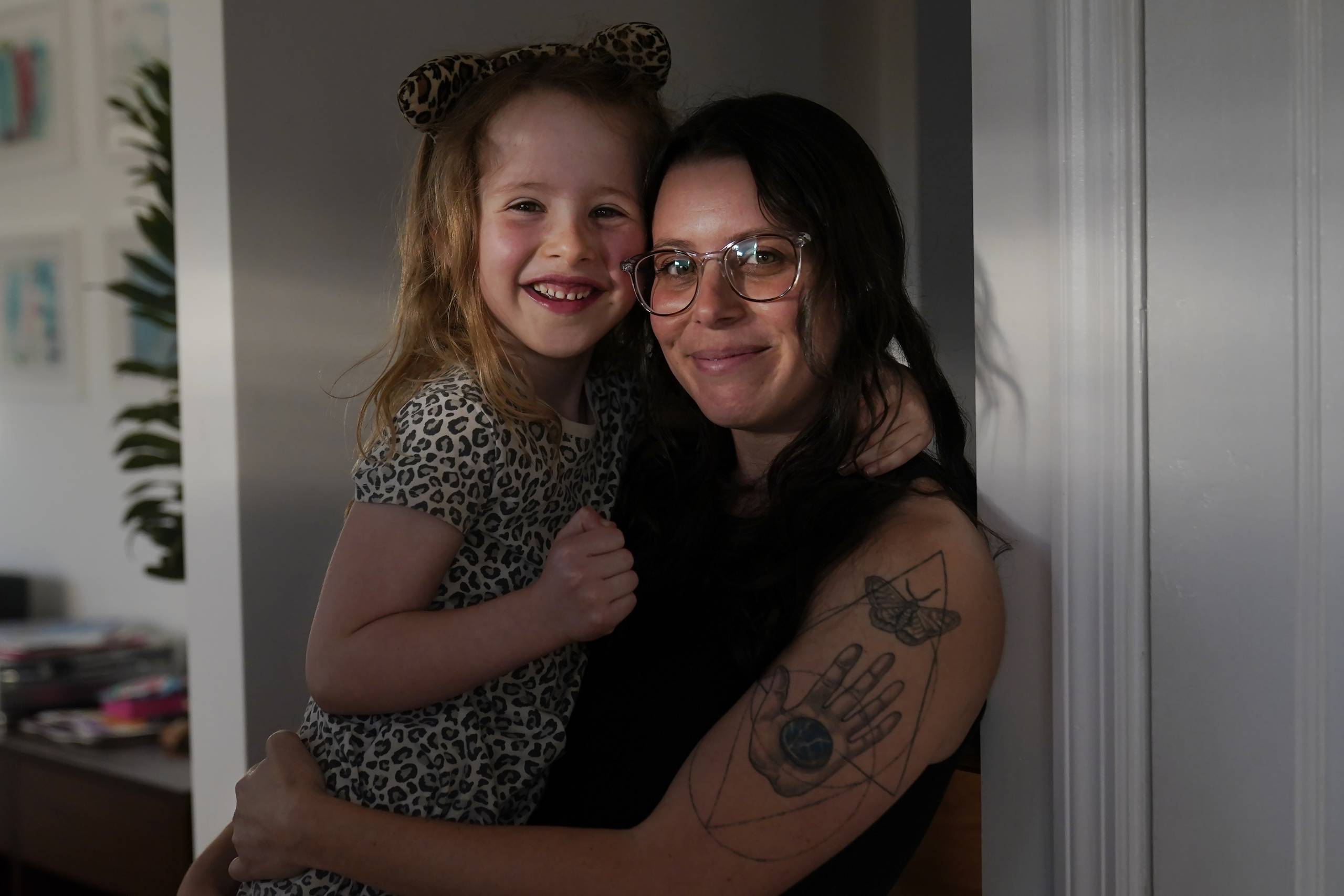 A white woman with glasses holds a child in her arms in a building.