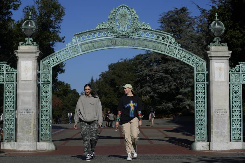 Two women walk on a campus through a metallic-green gate.