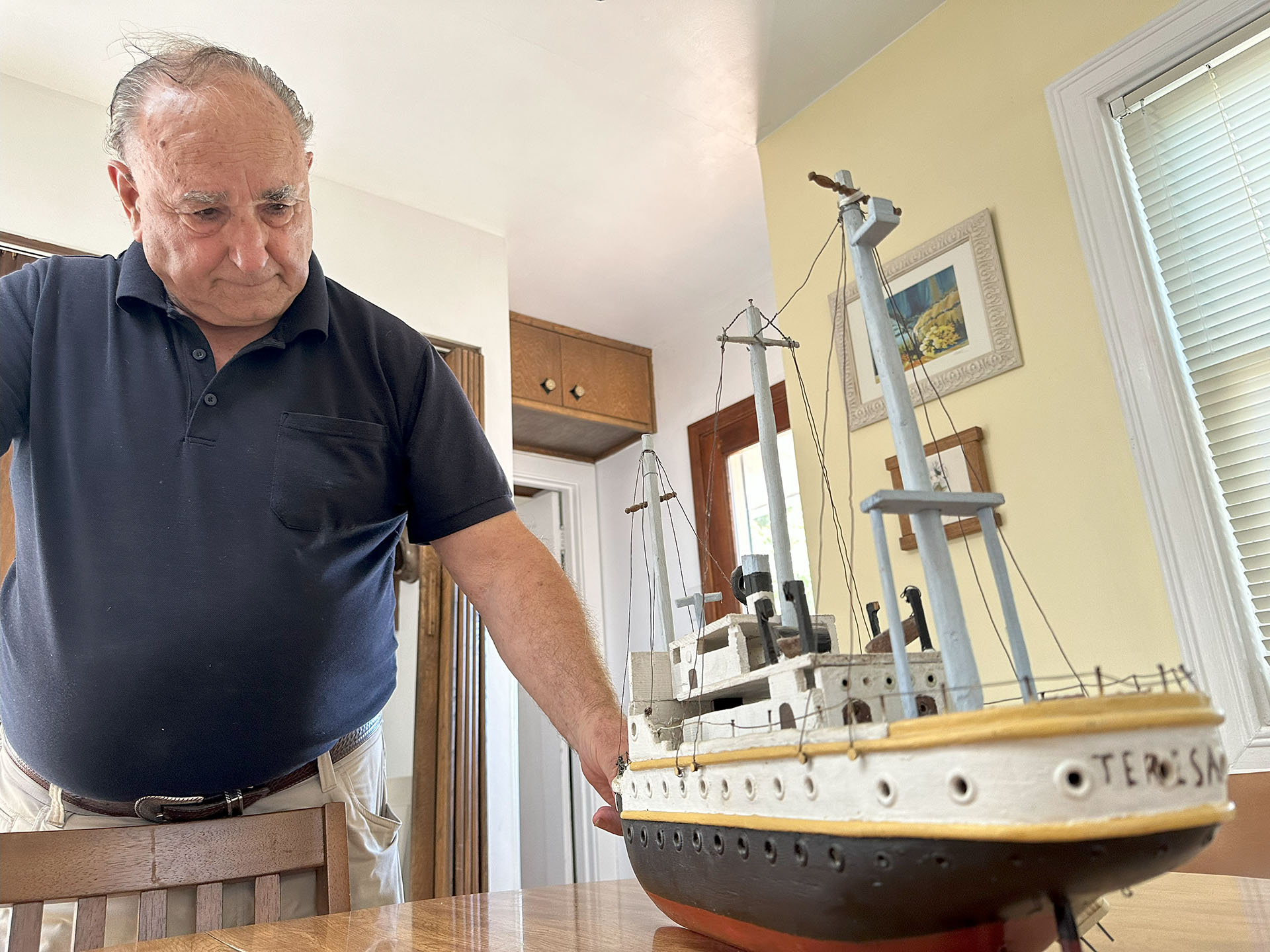 A man looks at a model boat on a kitchen table.