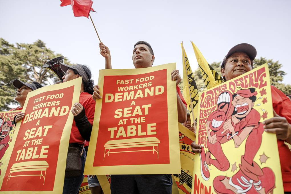 Men and women hold signs that say, "Fast Food Workers Demand A Seat At The Table."