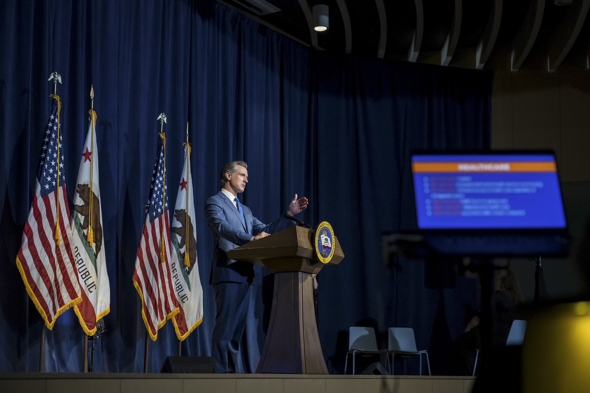 Gov. Gavin Newsom at a podium with an American and California flag behind him.