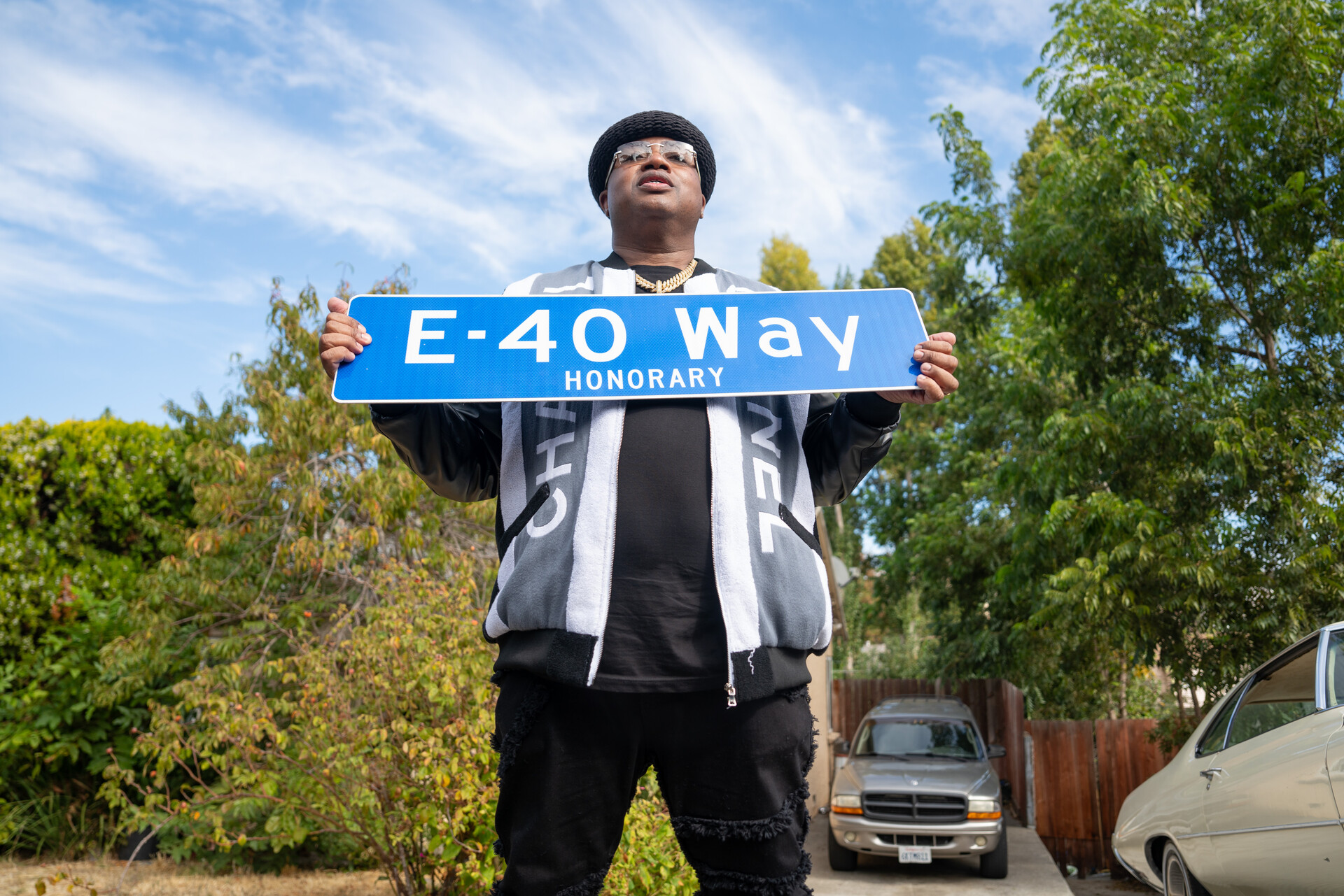 An African American man holds a sign up that says "E-40 Way."