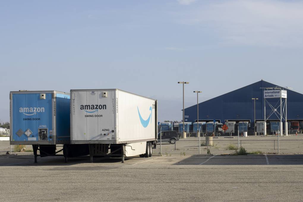 A view of an airport with a hangar in the background and two trucks in the foreground with "Amazon Prime" written on them.