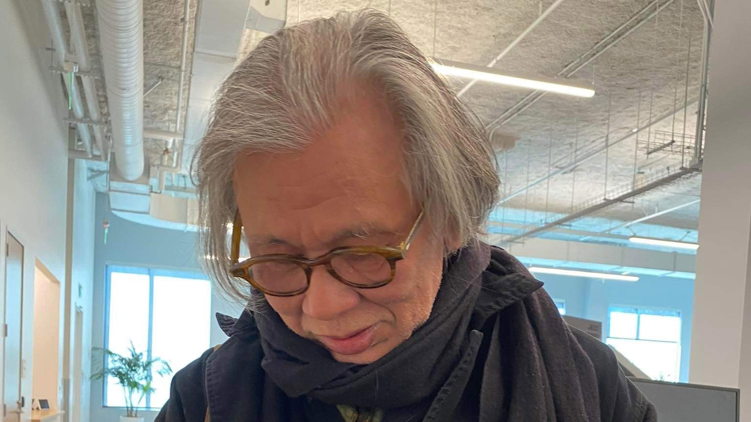 A grey-haired person with glasses looks down.