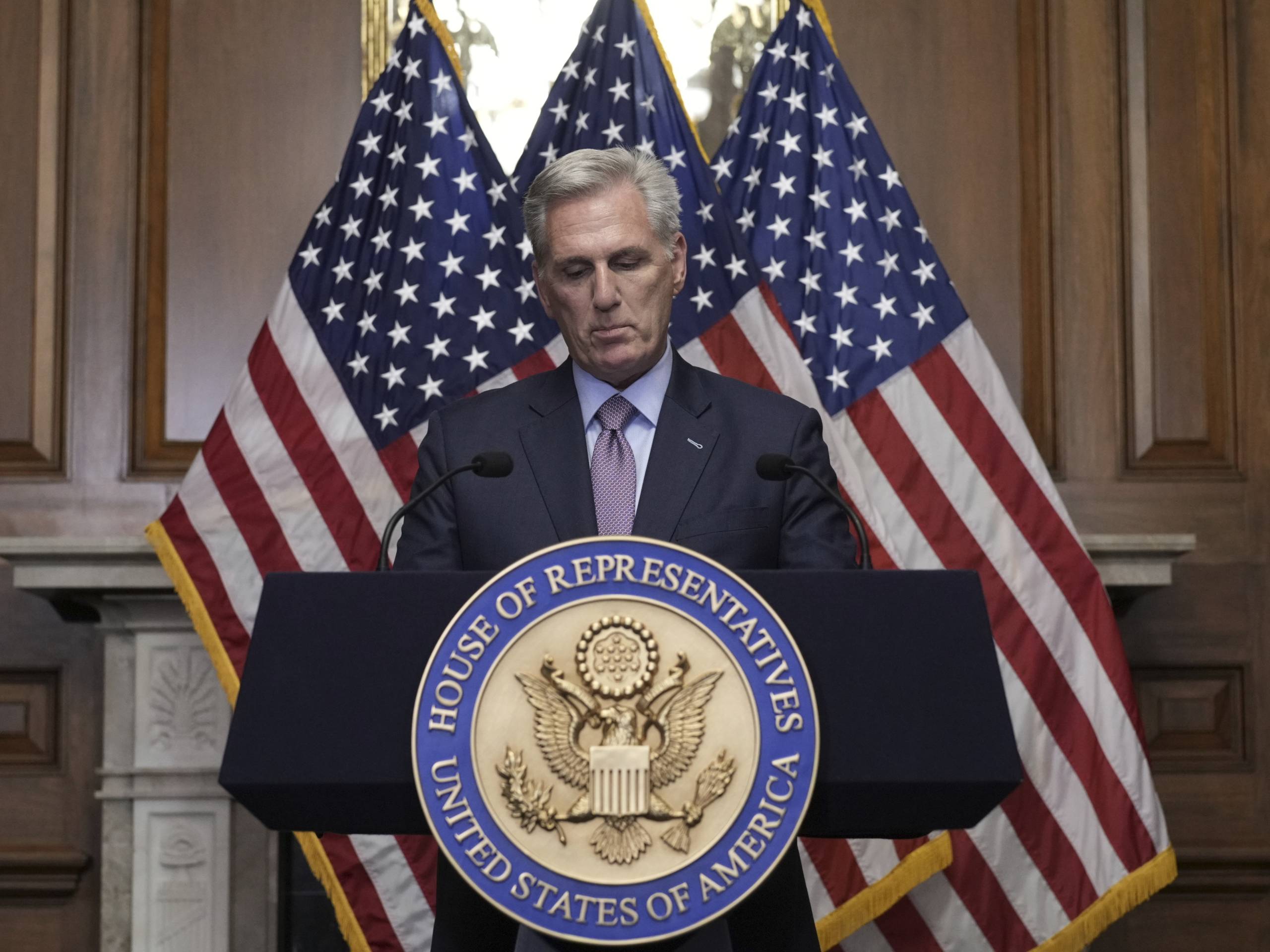 Former House Speaker Kevin McCarthy stands at a lectern with a House of Representatives plaque on it.