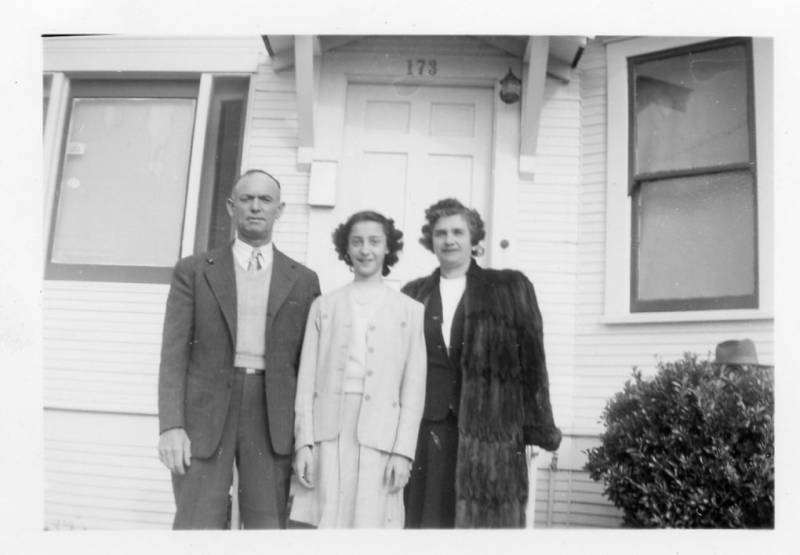 A black and white photograph from the 1940s of man, woman and child in front of a home.