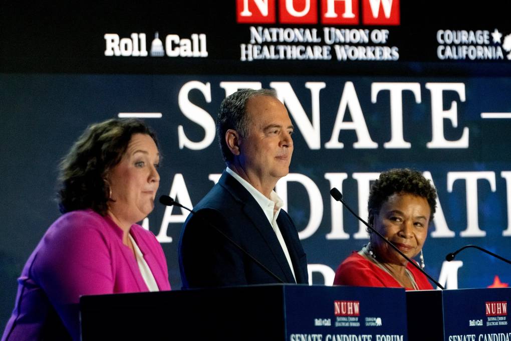 A woman, a man, and another woman stand side by side, each behind a lectern with microphones; behind them, it partially reads "Senate Candidates."