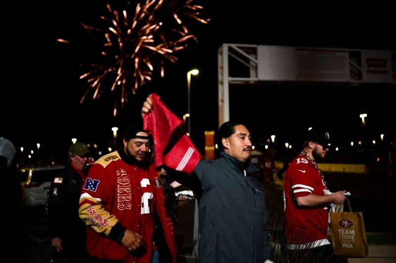 Fireworks are seen at night as people walk away wearing San Francisco 49ers paraphernalia.