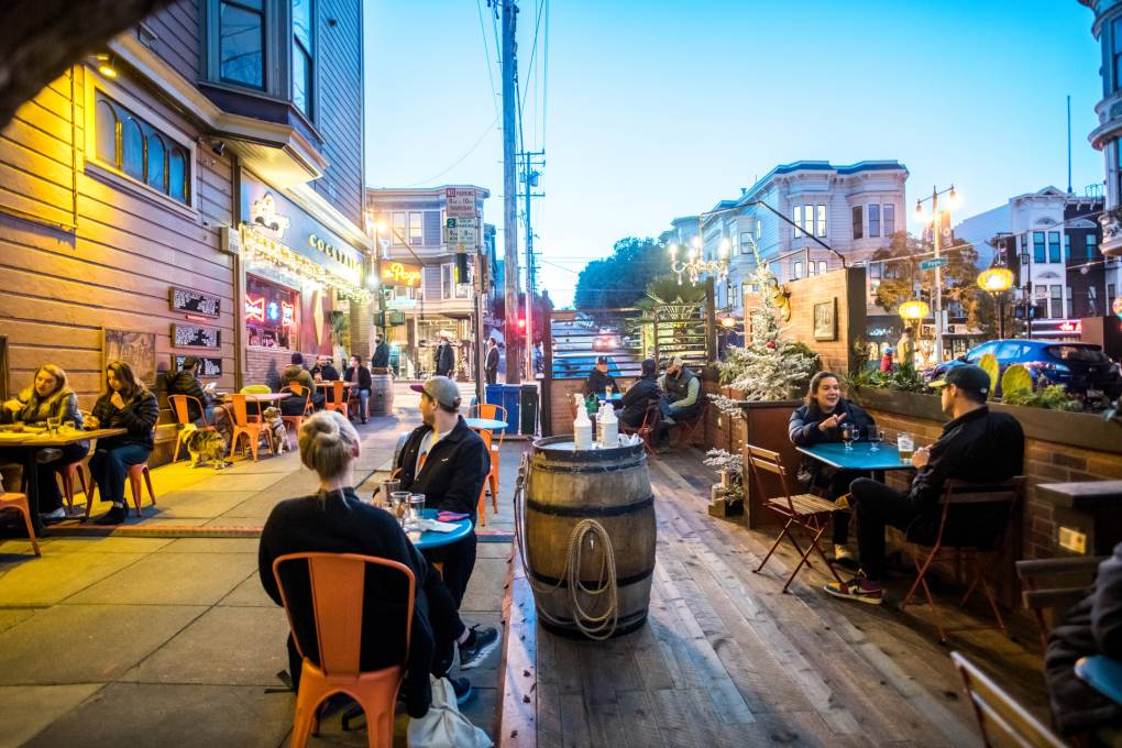 A street with a parklet on an evening with people sitting and drinking.