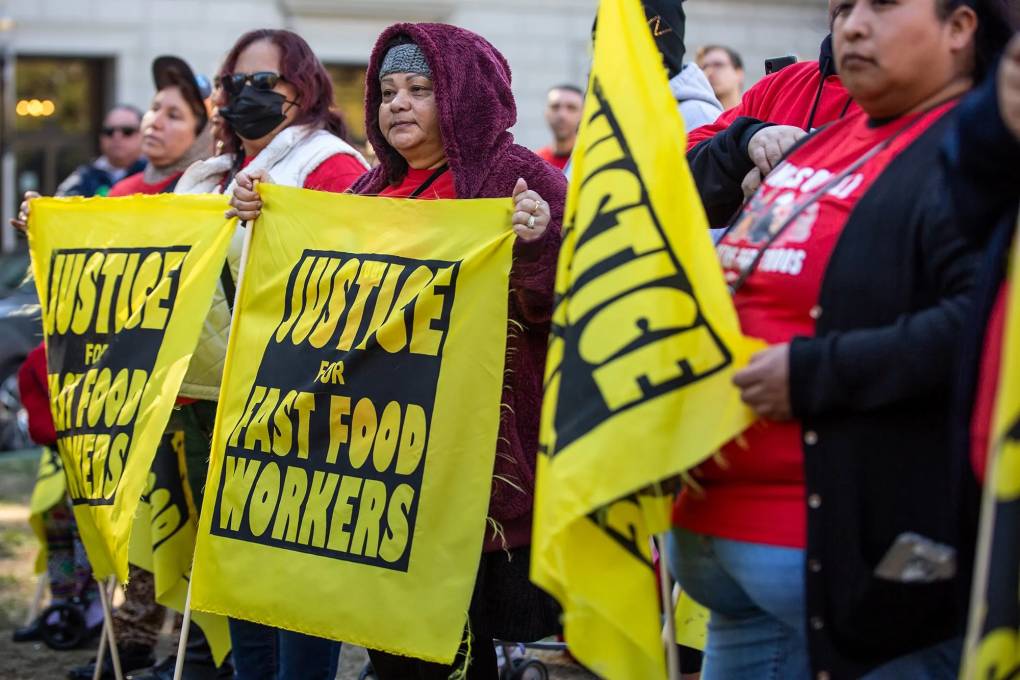 Protesters with yellow signs saying "Justice for Fast Food Workers" stand at a picket line.