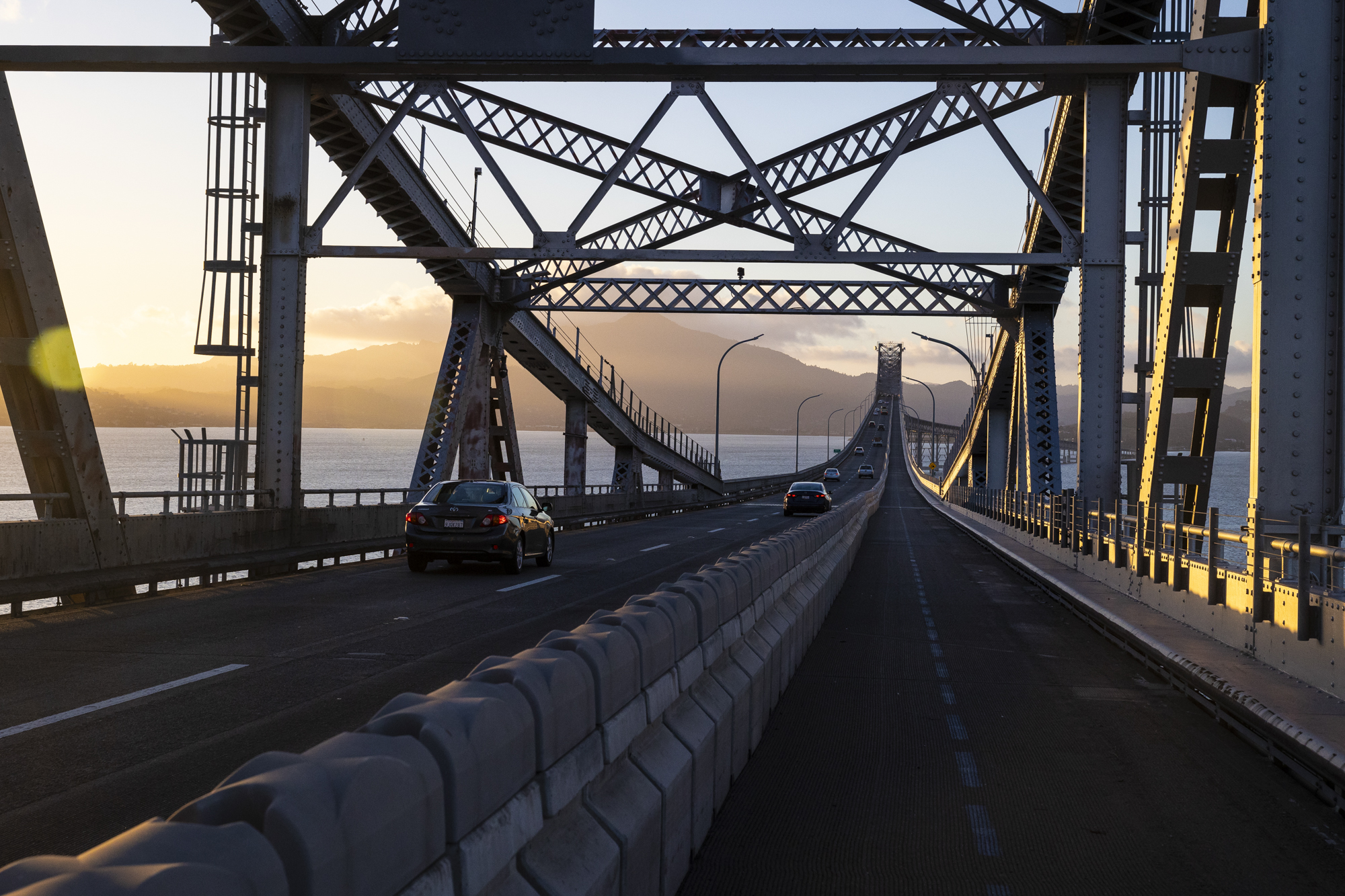 A bike lane on a large bridge on which cars are also driving.