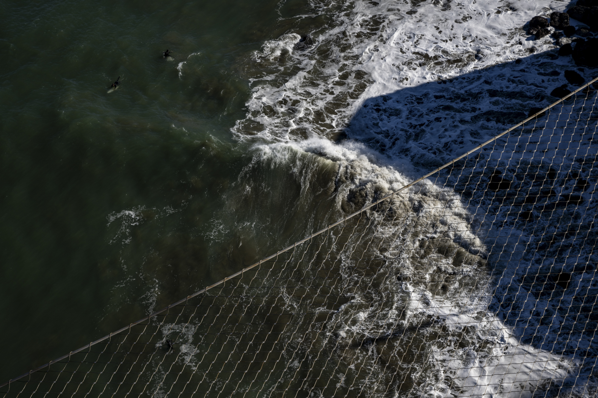 Swirling ocean waters with nets in foreground seen from above, on a bridge.