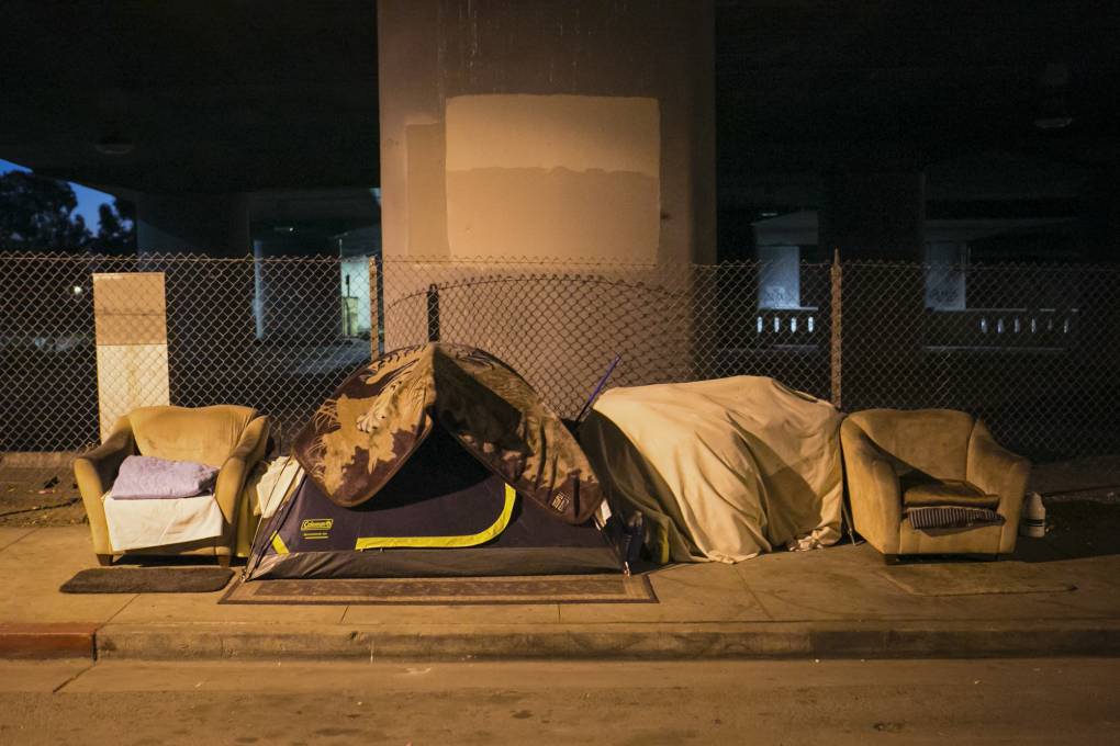 A tent and several armchairs under a freeway overpass at night.
