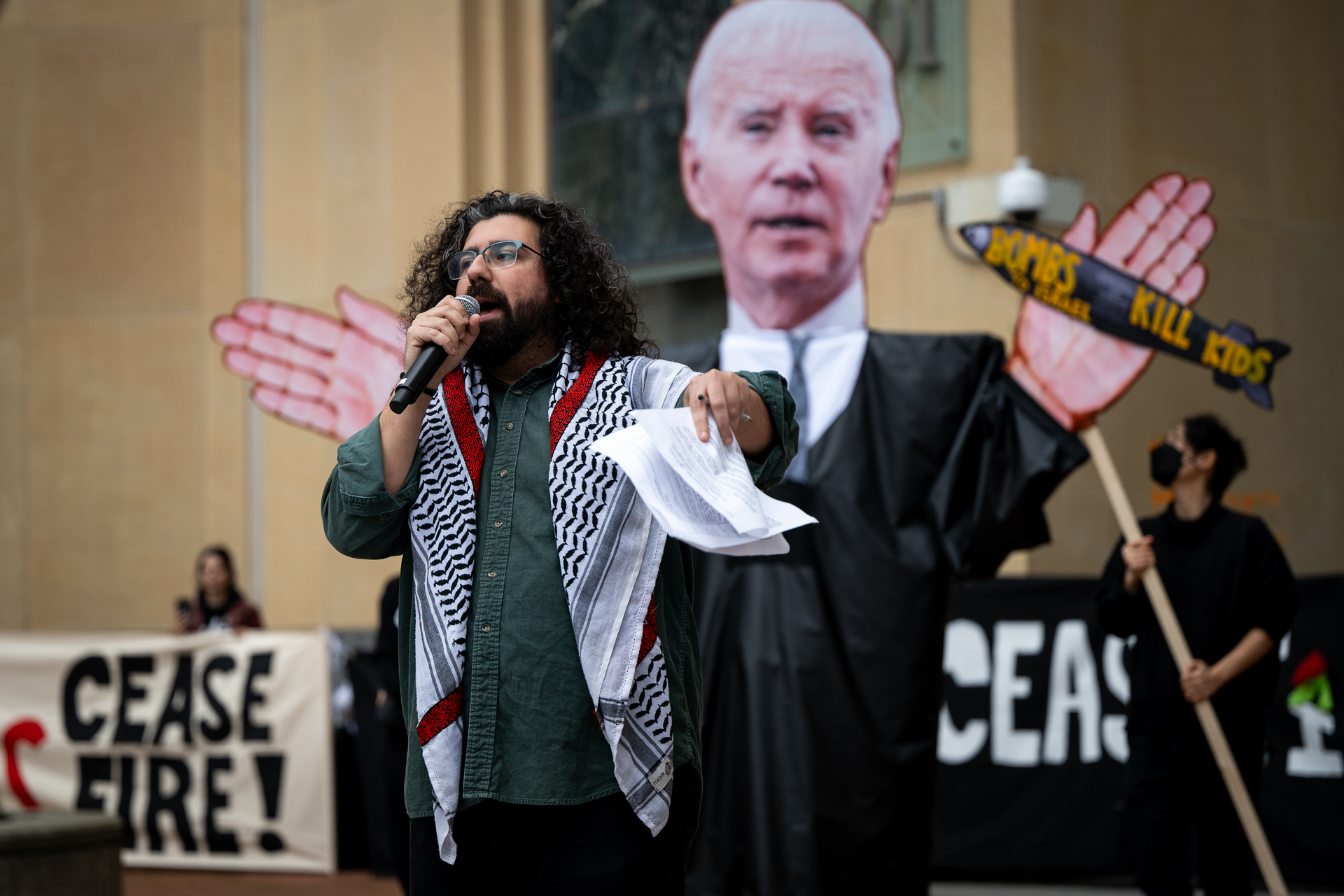A man with a microphone stands in front of a giant poster of President Joe Biden