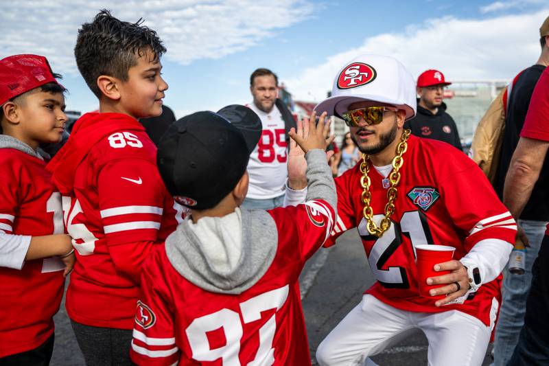 A young boy high fives a man with several people dressed in San Francisco 49ers sports jerseys.