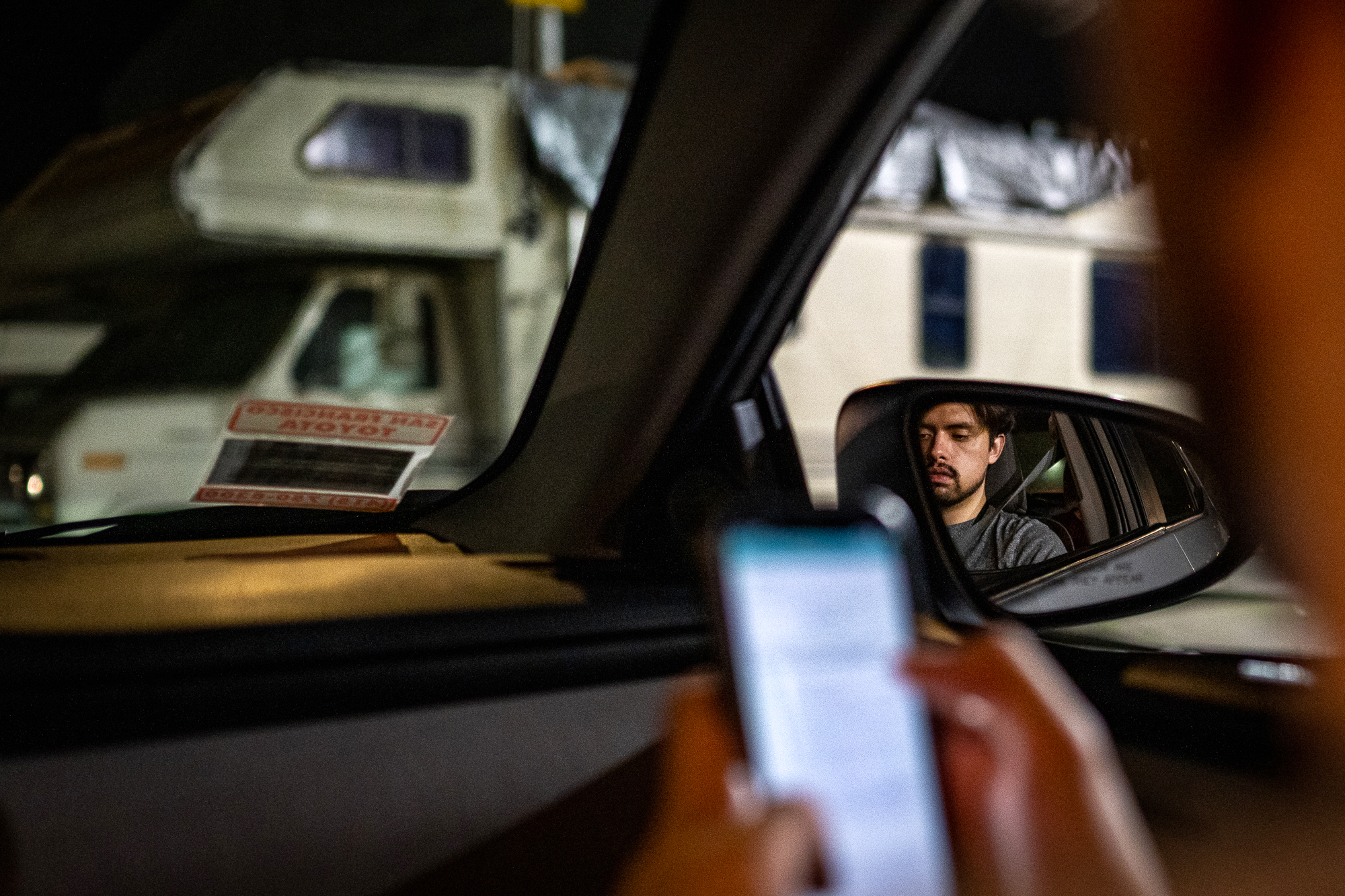 A man inputs data into a phone, while sitting in the passenger seat of a car