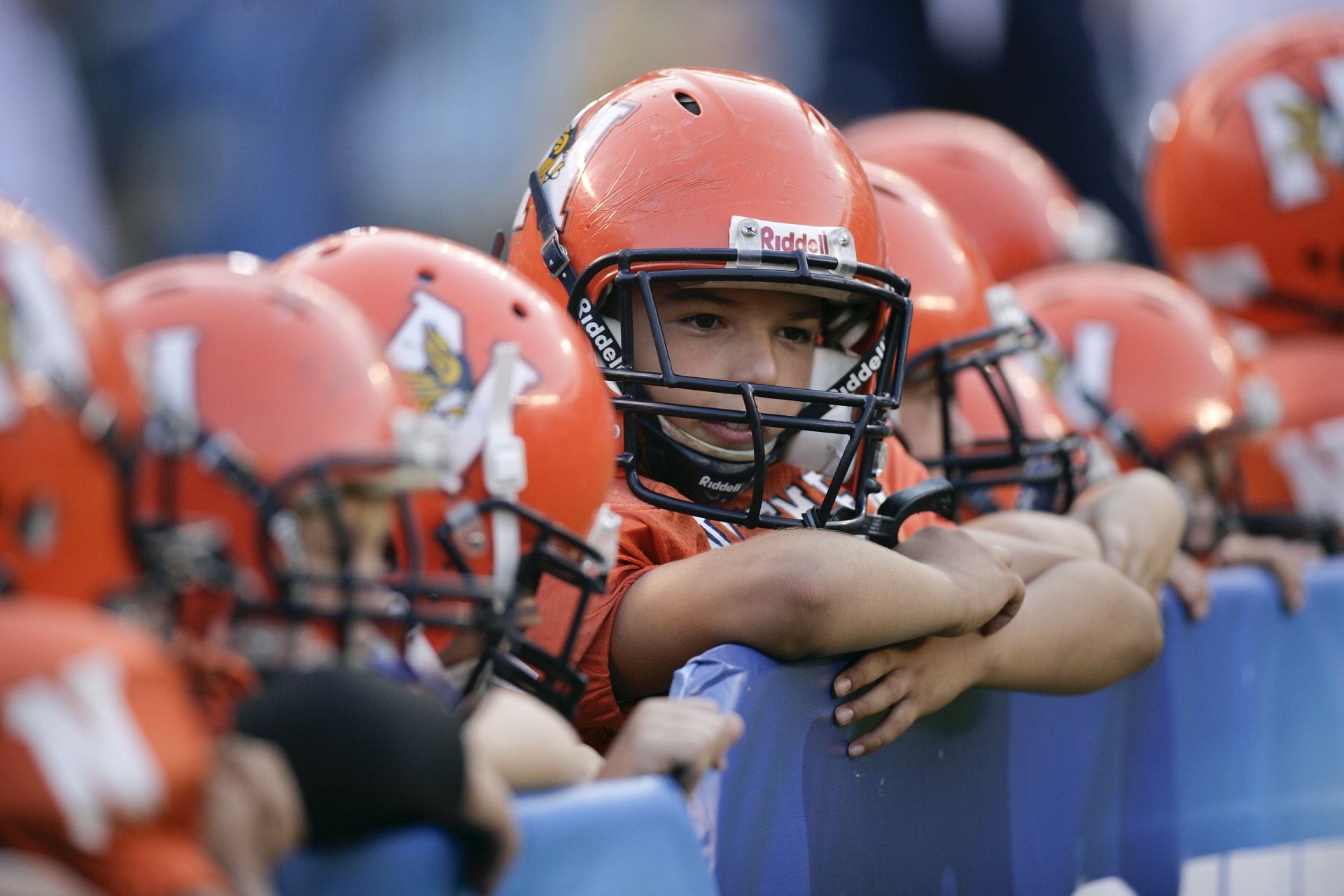 Young boys in orange football uniforms lean over a short wall.