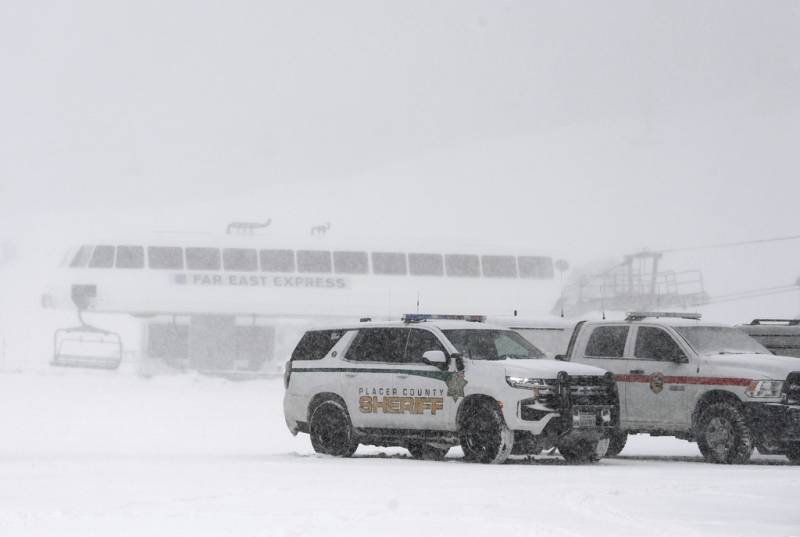 Several police cars parked in front of a ski lift with snow falling all around.