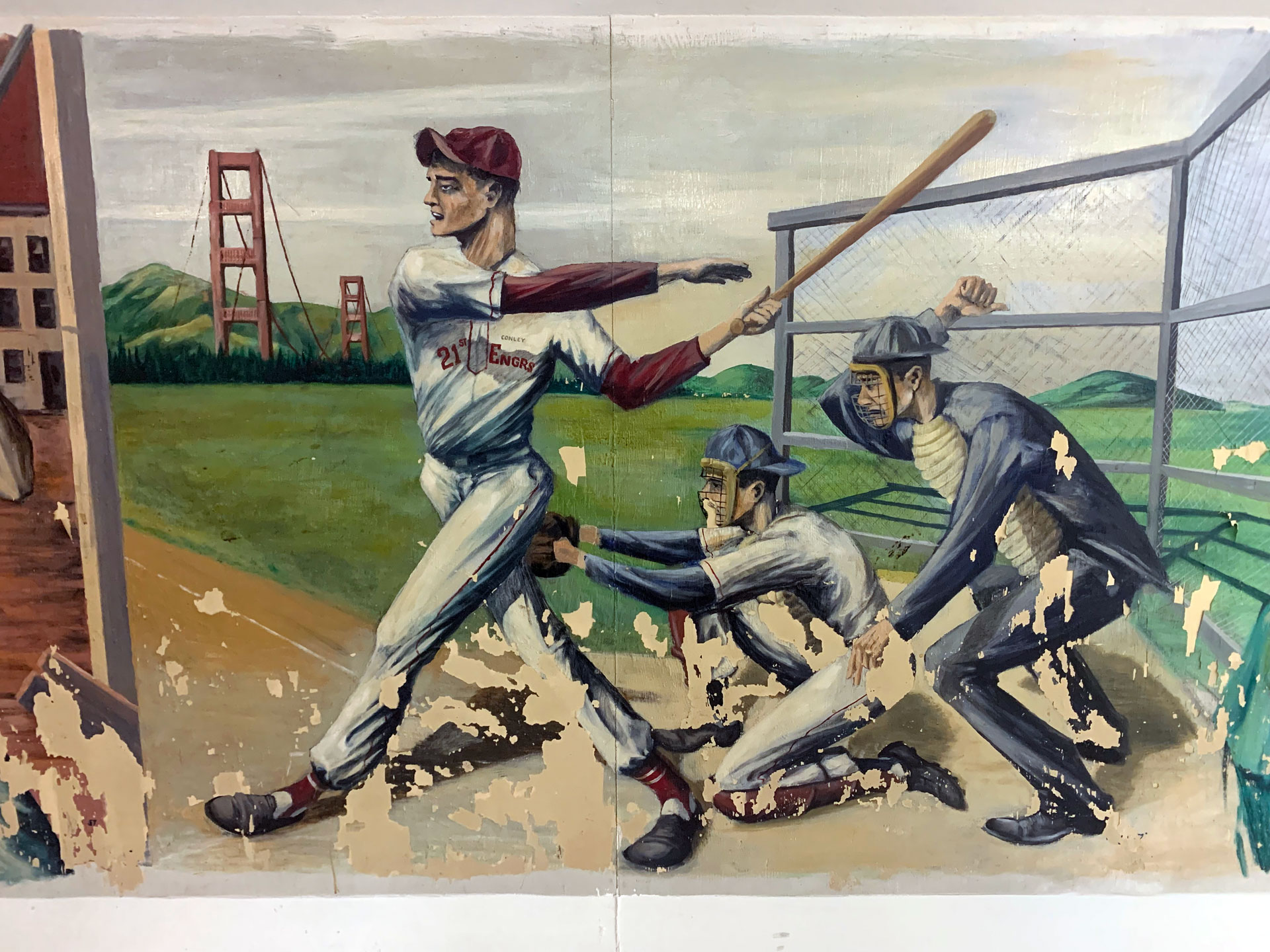 A slightly chipped mural depicting a batter, catcher and umpire at home plate. Behind them loom two towers of the Golden Gate Bridge.