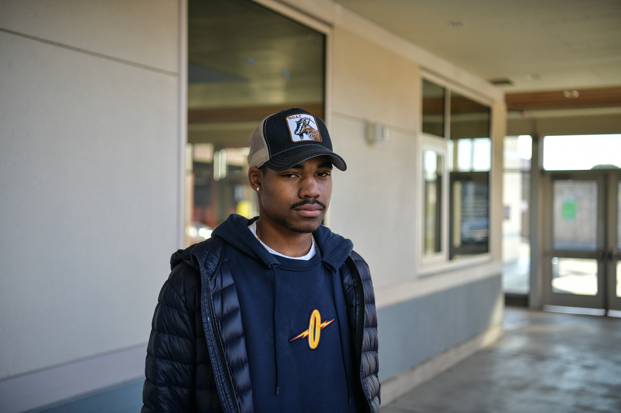 A teenager with a baseball hat stands in front of a classroom.