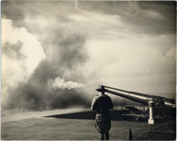 Outline of a man in old fashioned military uniform stands next to a cannon pointed a soupy mass of clouds.