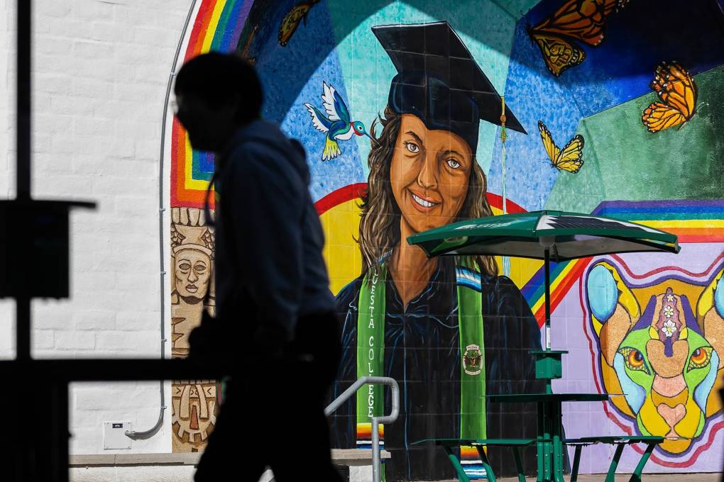 The outline of a student walking in front of a colorful mural depicting a smiling female student at graduation.