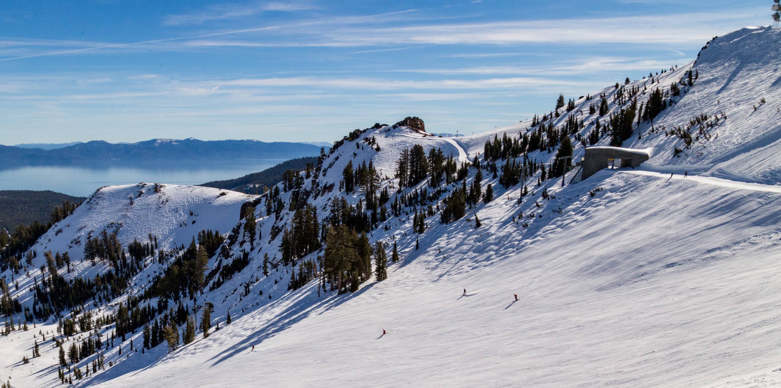 an aerial view of three people skiing across a slope of a mountain with a lake in the background