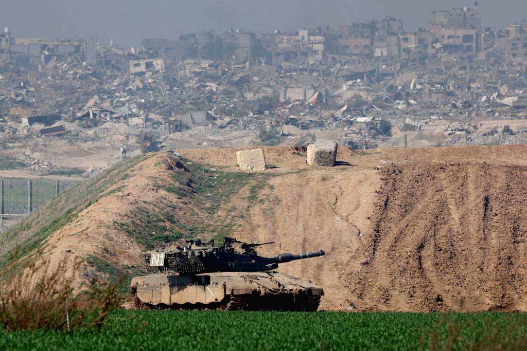 A tank in the foreground with a hill and buildings in the background.