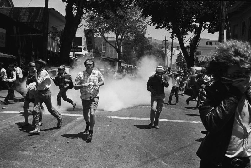 Black and white photo of several people running on a street with smoke behind them.