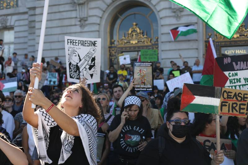 Pro-Palestinian protesters, many waving Palestinian flags and wearing headscarves, protest in front of San Francisco City Hall.