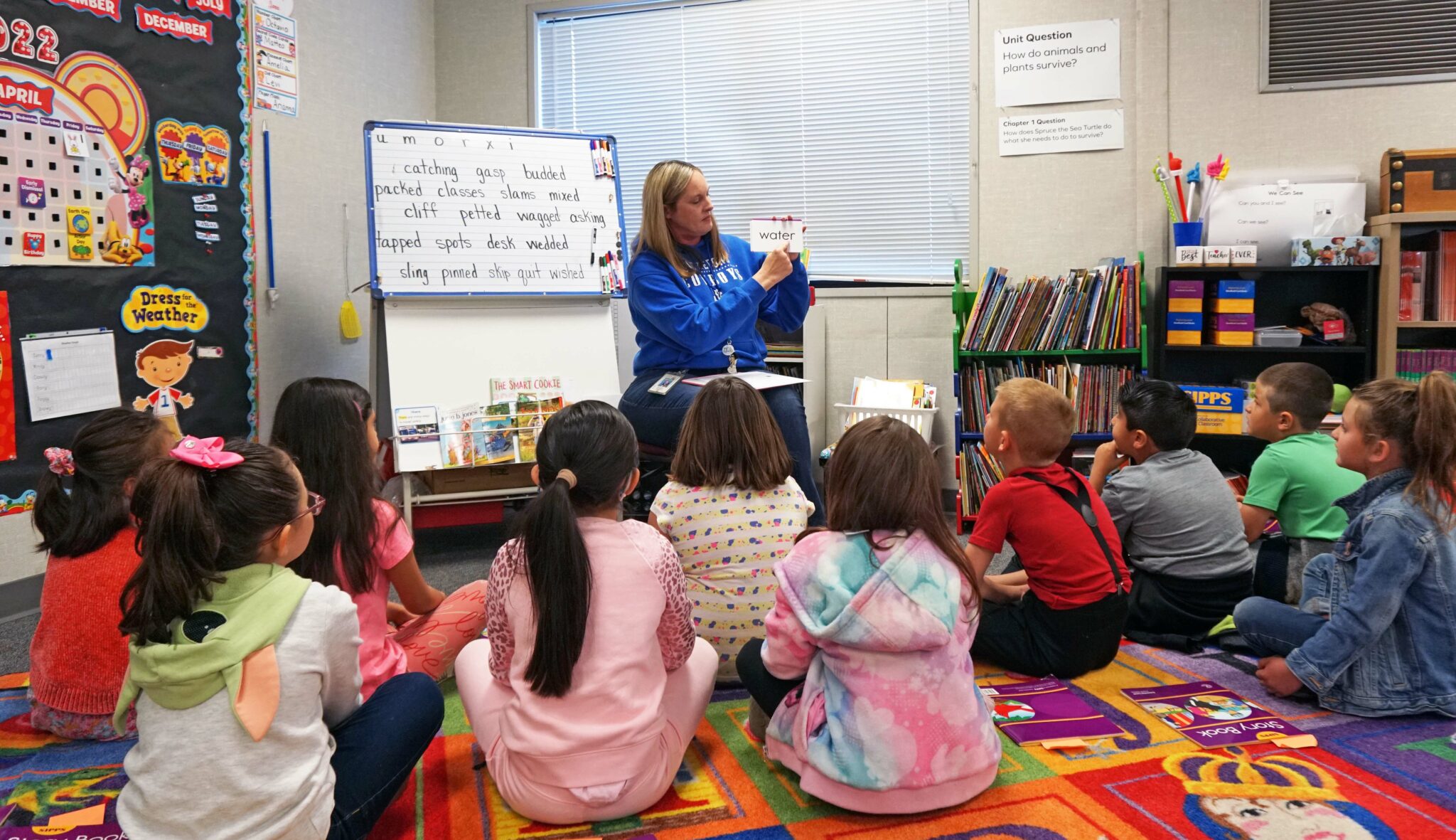 A teacher and students sitting on the floor in a classroom, elementary school.