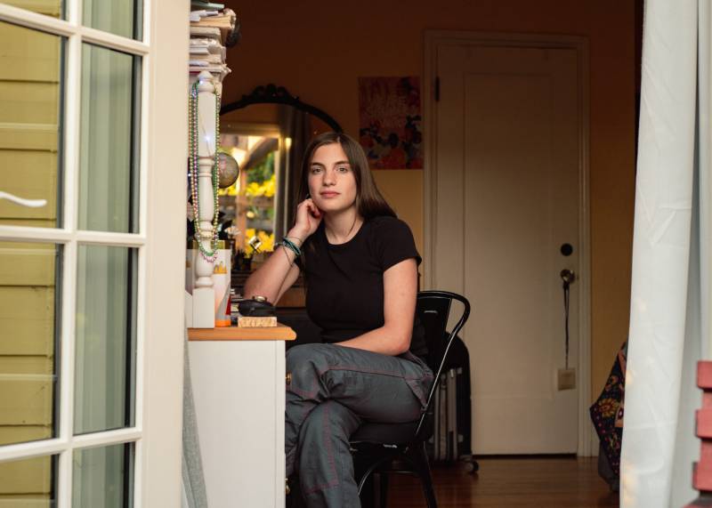 A white woman wearing a black shirt sits in a chair in a home, with her right arm resting on the desk.