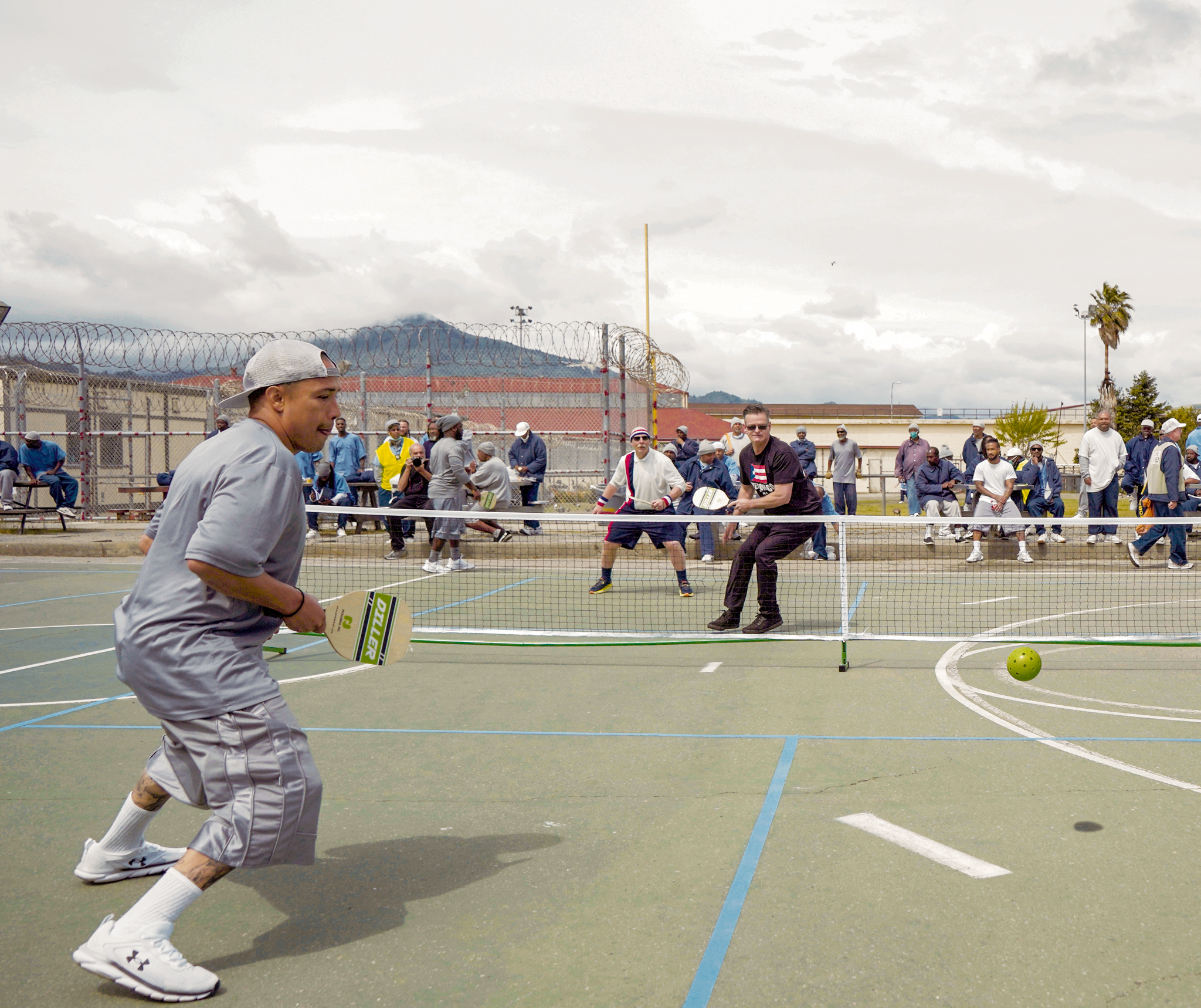 Men in a prison yard play pickleball.