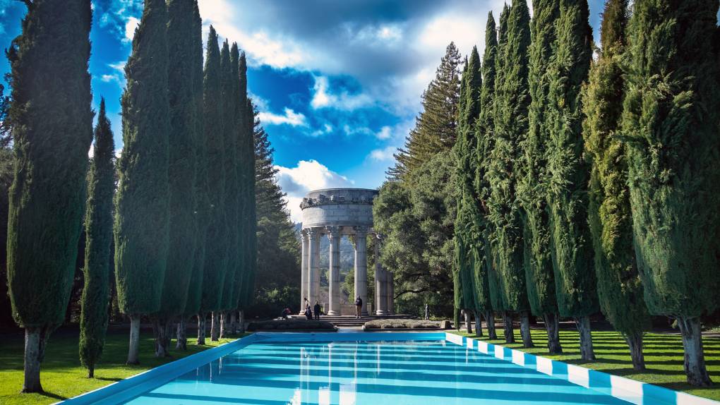 A row of poplars line an aquamarine pool. At the end is a round, classical-looking building with columns.