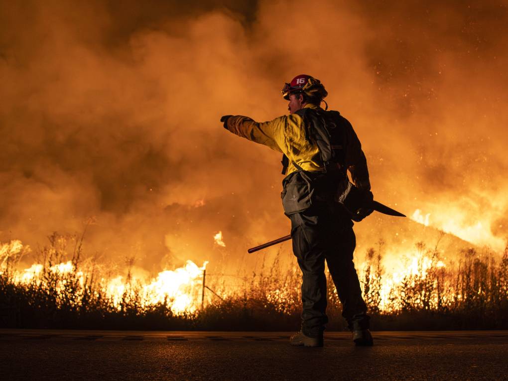 A firefighter stands in front of a burning wildfire.
