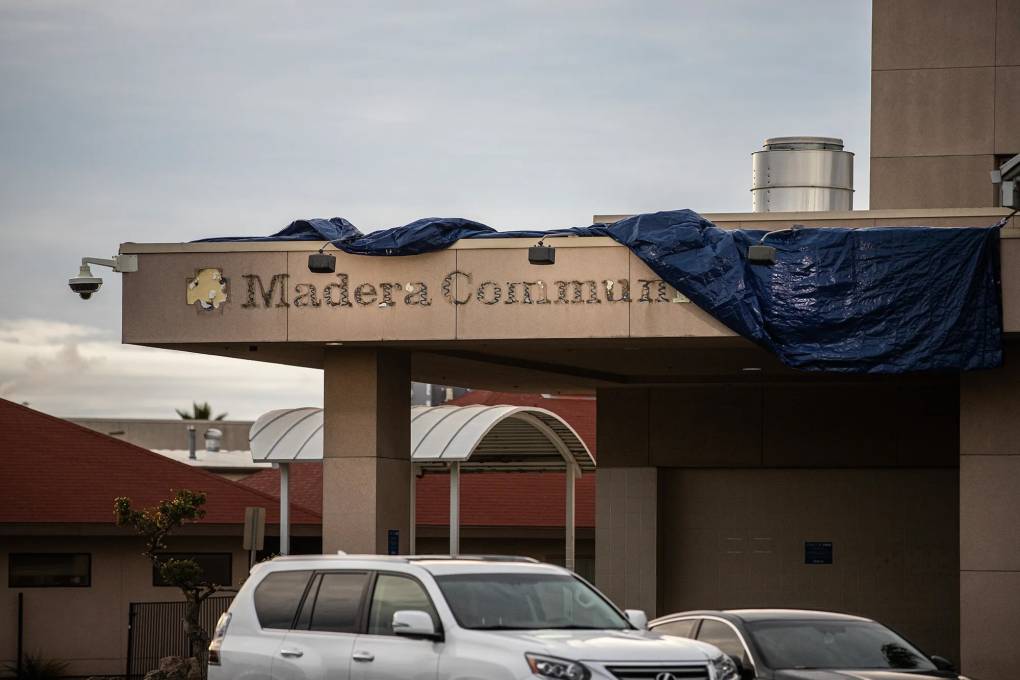 A rundown building with tarps partially covering the entrance where the words "Madera Community" can be seen.