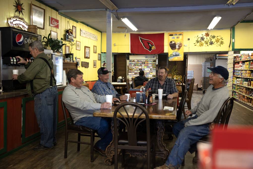 Five men sit at a table in a store with yellow walls.