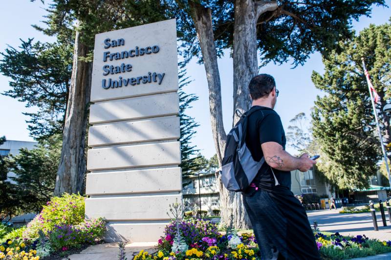 a student walks in front of a San Francisco State University sign on campus