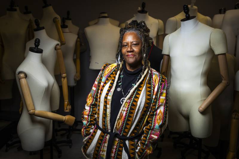 African American woman stands among mannequins as she smiles at the camera.