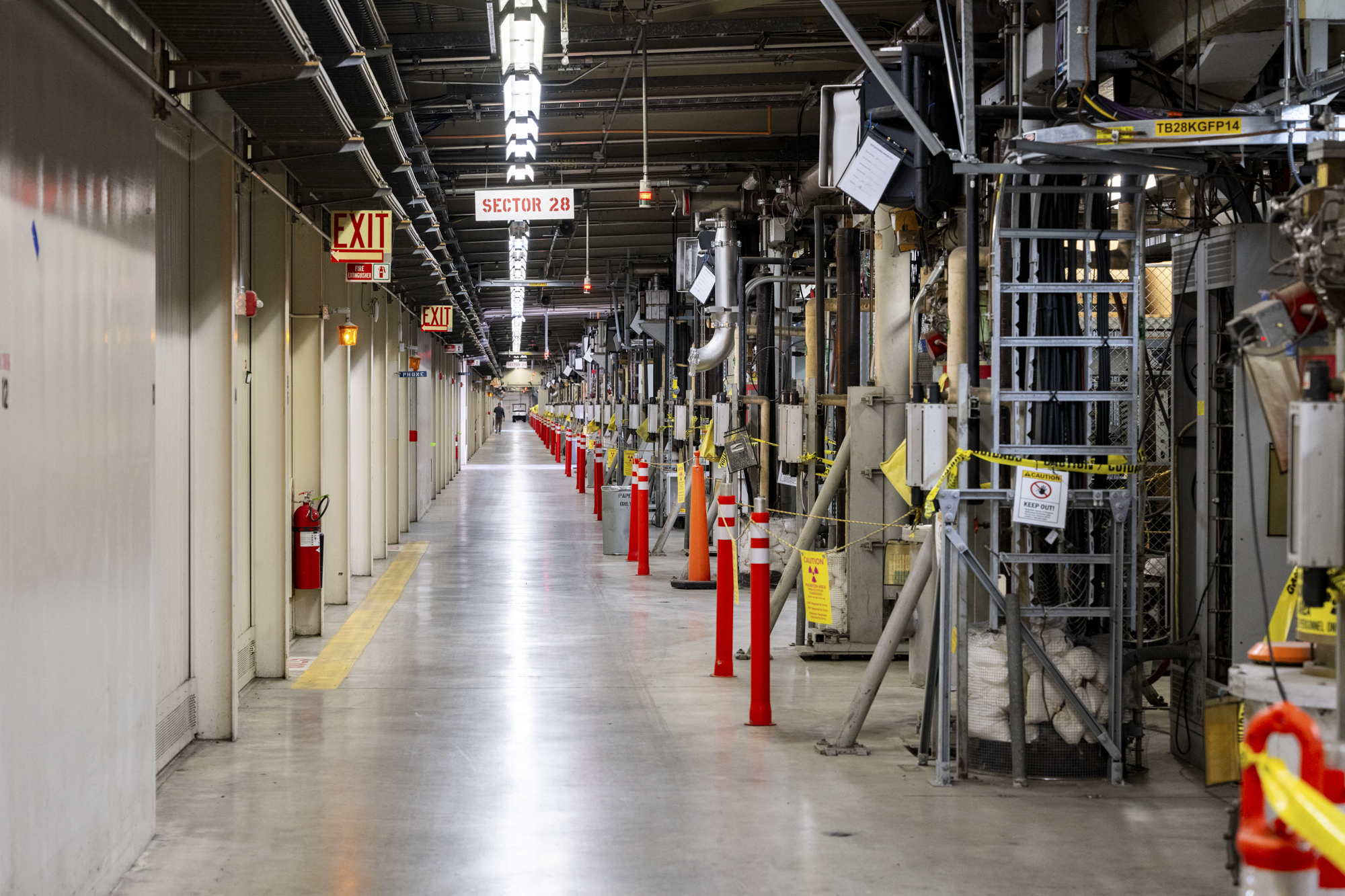 A long room that you cannot see the end of. It is about 20 feet wide. On the left is a walkway for people and small vehicles. On the right side of the image, is the linear accelerator equipment, which looks like a lot of tubes and wires.
