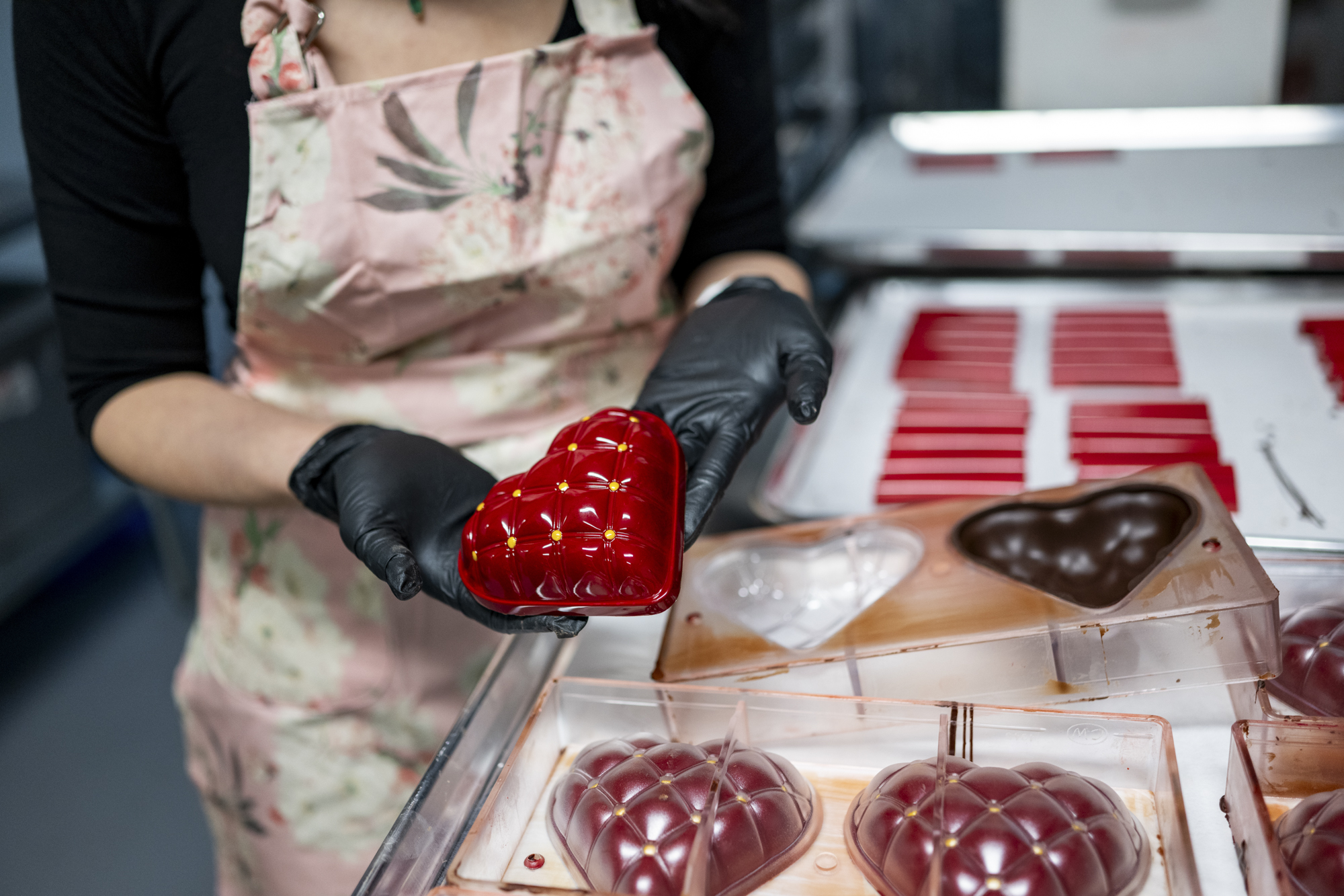 Pair of gloved hands hold a red heart shaped mold for making chocolates.